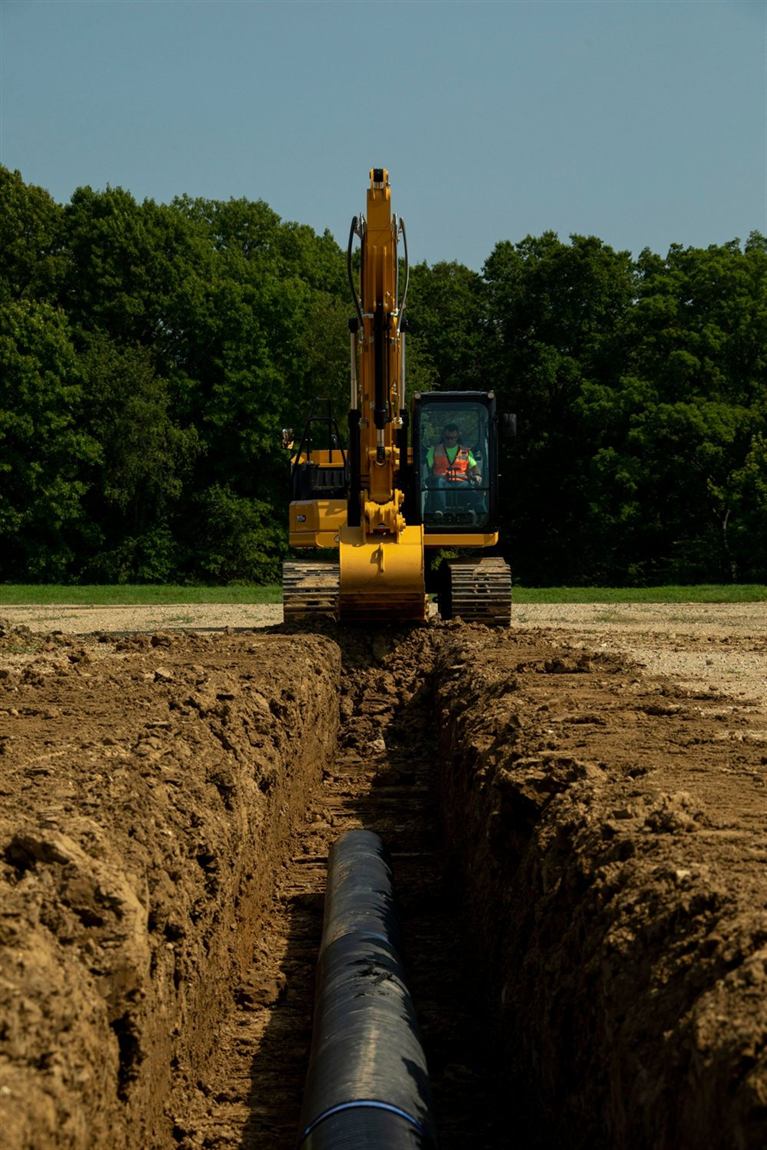 Excavator trenching for underground utilities with pipe laid in